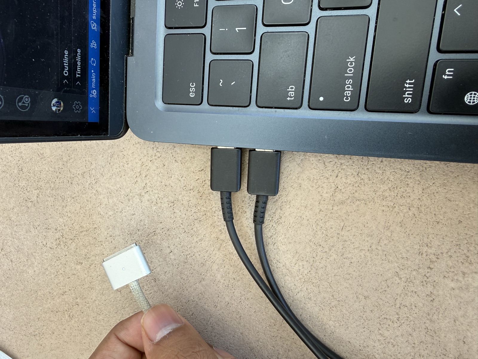 The same USB-C cable now plugged into both left-side ports of the MacBook, connecting the laptop to itself. The MagSafe charger is still held in the other hand, disconnected.